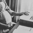 Woman holding baby bump sat at a desk using a laptop
