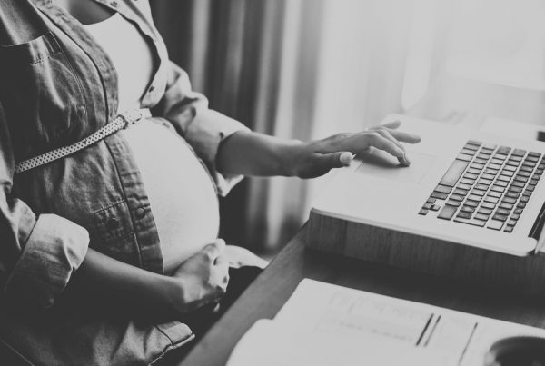 Woman holding baby bump sat at a desk using a laptop