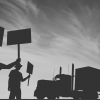 People in workwear holding picket signs in front of a truck.