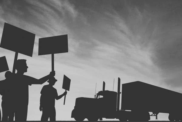 People in workwear holding picket signs in front of a truck.