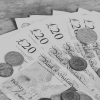 Image of multiple twenty pound notes on a table with coins on top