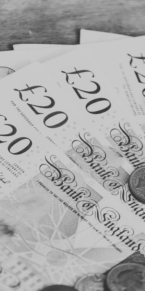 Image of multiple twenty pound notes on a table with coins on top