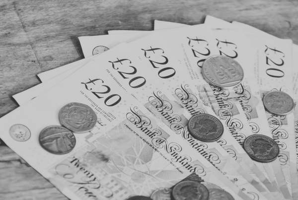Image of multiple twenty pound notes on a table with coins on top