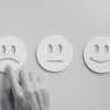 Three face cut outs in card with a hand pointing at the upset face