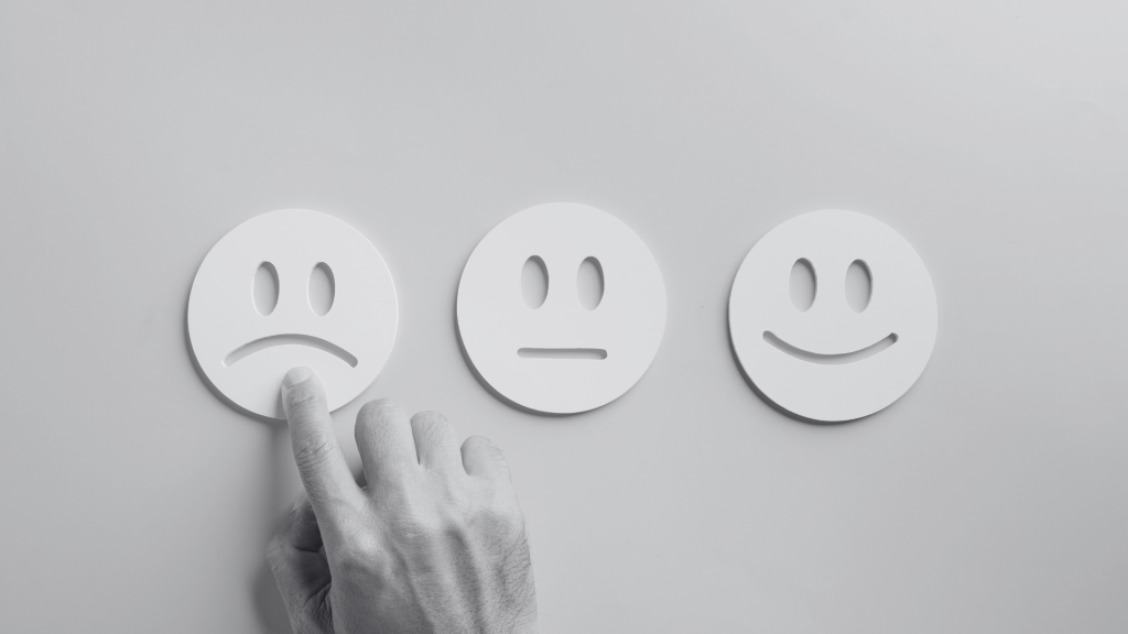 Three face cut outs in card with a hand pointing at the upset face